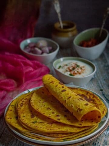 Besan masala roti or gram flour roti is stacked on a plate with the top one rolled in half.