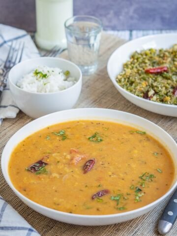 Arachuvitta sambar displayed on a white shallow bowl with broad beans curry and a bowl of rice with buttermilk.
