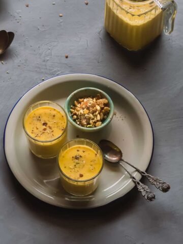 2 glasses of yellow pumpkin payasam served on an enamel plate.